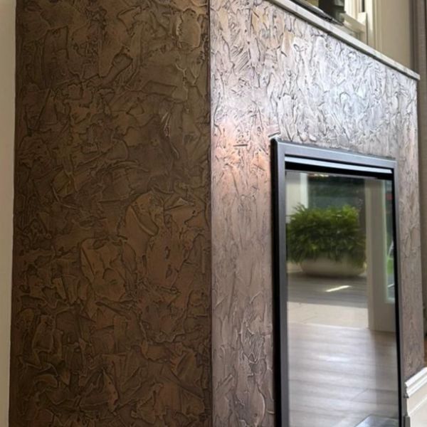 Textured wall corner with dark and light brown finishes next to a window.