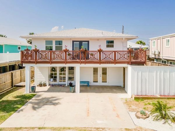 Exterior view of a renovated two-story coastal home featuring a wraparound upper deck.