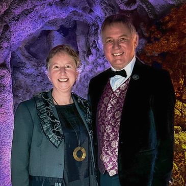 A smiling couple dressed in formal attire with a colorful cave-like background.