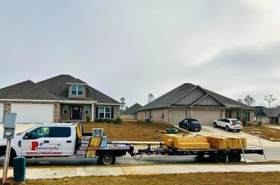 Roofing company truck with materials parked in front of houses.
