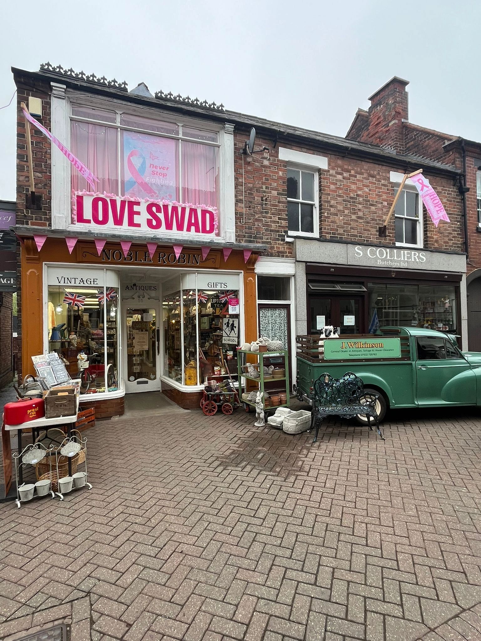 Vintage shop with pink cancer awareness decorations and a green antique truck outside.