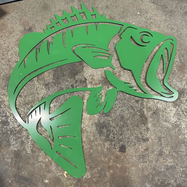 Green metal fish wall art with an open mouth on concrete.