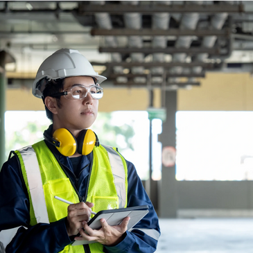 Construction worker in safety gear using a tablet on site.
