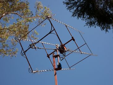 Large outdoor antenna against a clear blue sky with surrounding trees.