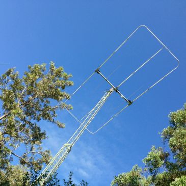 A tall antenna tower among green trees against a clear blue sky.