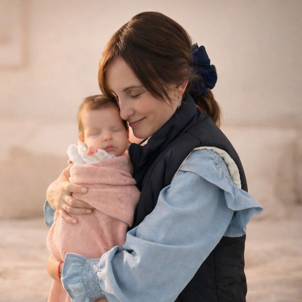 A woman gently hugging a sleeping baby wrapped in a pink blanket.