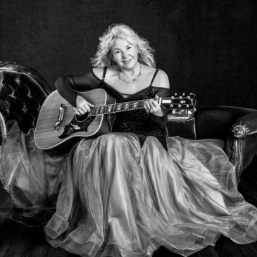 Woman playing acoustic guitar in a flowing dress.