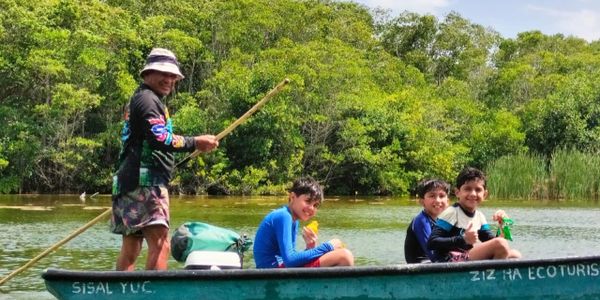 A man and three children enjoying a boat ride on a sunny day near lush greenery.