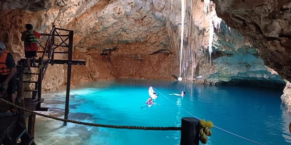People swimming in a bright blue underground cave pool.