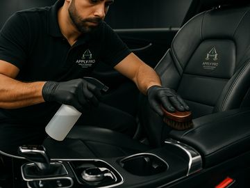 A professional cleaning the leather seat of a car with a brush and spray bottle.