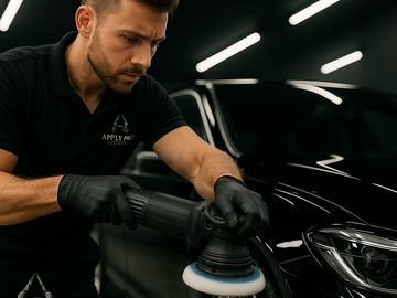 Man polishing a black car with a buffer in a professional detailing setting.