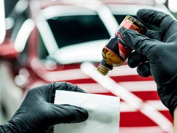 Person applying car detailing liquid with cloth near a red car.