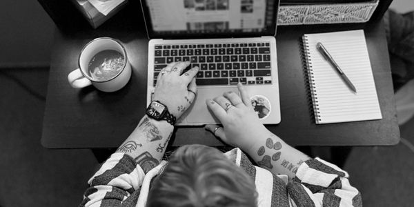 Top view of person working on laptop with tattoos and coffee nearby.