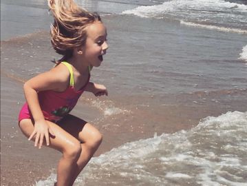 A little girl enjoying waves at the beach.