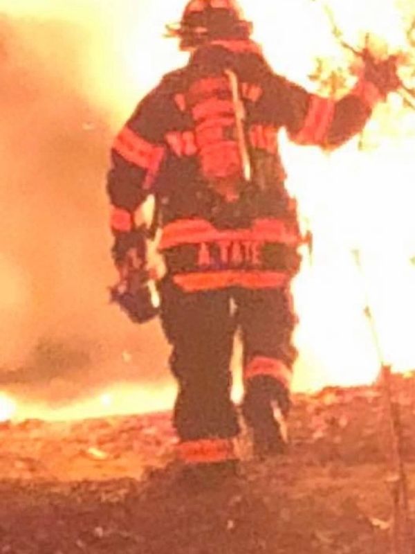Firefighter walking towards intense flames in full gear.