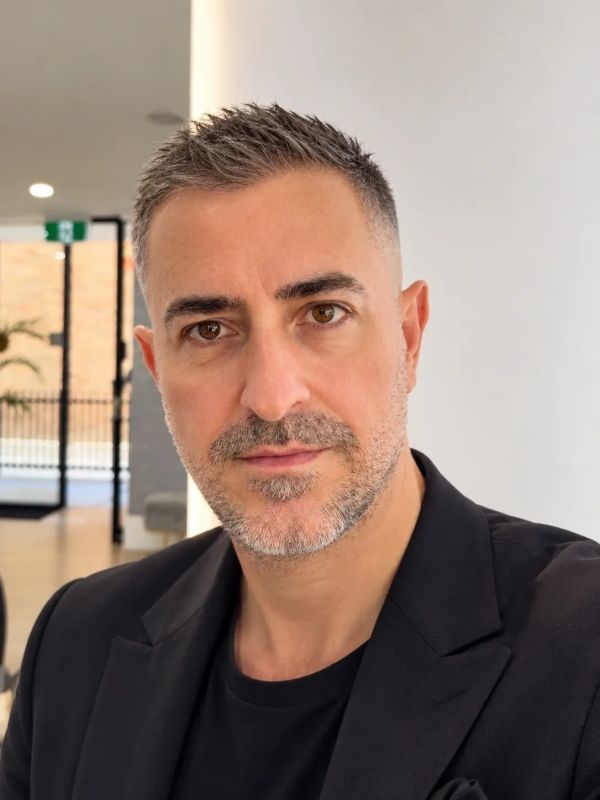 Man with short gray hair and beard in black jacket.
