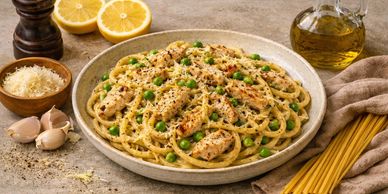 A bowl of chicken carbonara surrounded by ingredients like garlic, cheese, black pepper and pasta.
