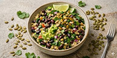 A bowl of healthy quinoa salad topped with black beans, pumpkin seeds, and lime wedges.