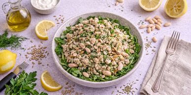 A fresh green salad topped with nuts and herbs on a white table.