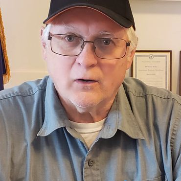 Older man wearing glasses and a black cap indoors.