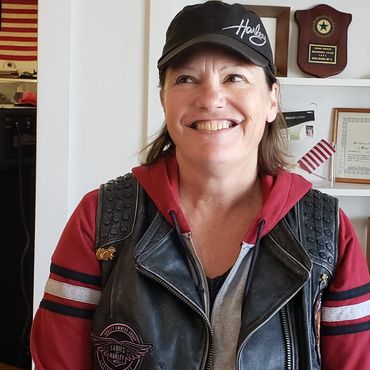 Smiling woman in a Harley jacket and cap indoors.