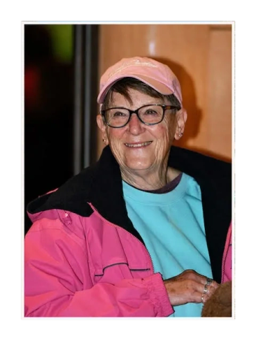 Smiling elderly woman in glasses and pink jacket.