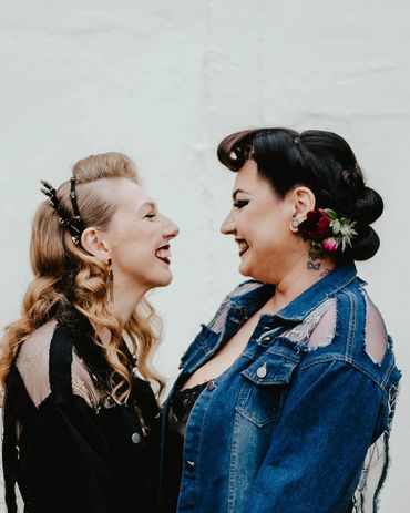 Two women smiling and facing each other, dressed in stylish, edgy clothing.