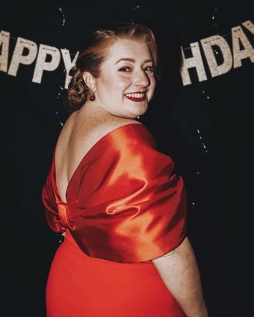 Woman in a red dress smiling at a birthday party.