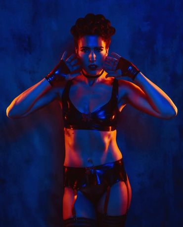 Person in black leather outfit posing with hands near face under dramatic lighting.