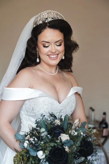 Newlywed Katherine smiling looking down at bouquet. Hair styled in Hollywood Waves.