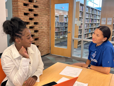 Two women engaged in a friendly conversation at a library table.