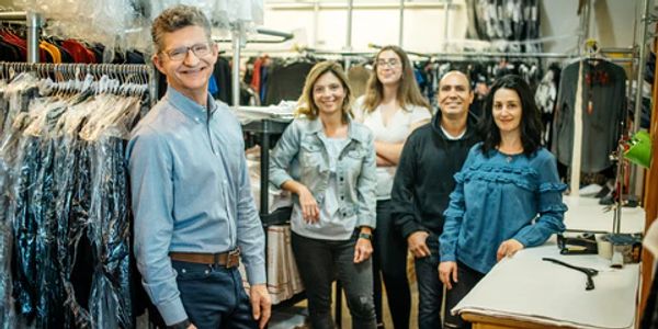 A group of five people smiling in a clothing store or dry cleaning shop.