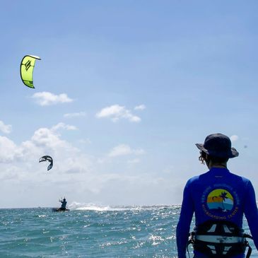 Person watching kitesurfers on the ocean under a clear blue sky.