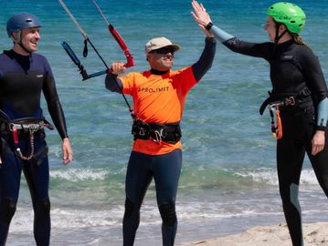 Three people in wetsuits and helmets enjoying kite surfing on the beach.