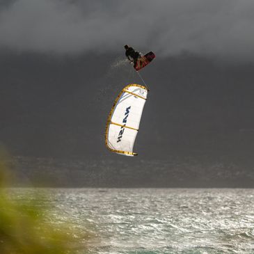 Person performing a high jump while kiteboarding over the water.