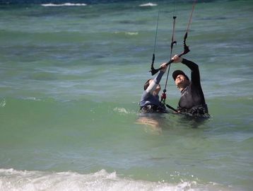 Two people in wetsuits learning kite surfing in the ocean.