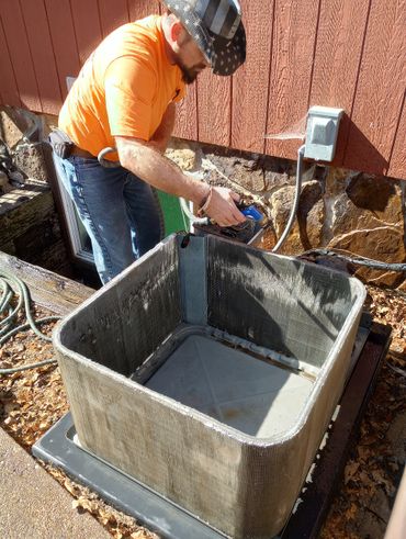 Man in an orange shirt working on an outdoor HVAC unit.