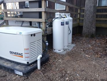 A Generac generator with three propane tanks outside a wooden deck.