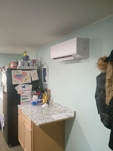 Kitchen corner with a refrigerator, countertop, and wall-mounted air conditioner.