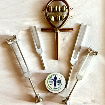 Various tuning forks and a copper ankh-shaped tuning device on a white surface.