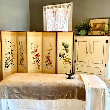 A cozy room with a massage table and decorative folding screen.
