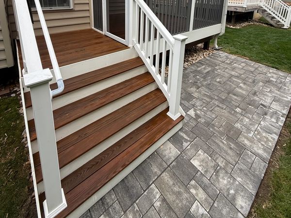 Wooden stairs with white railings next to a gray stone pathway.