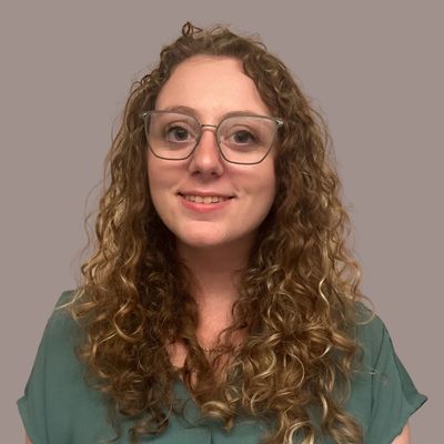 Smiling woman with curly hair and glasses against a plain background.