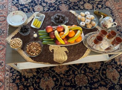 A table set with fruits, nuts, tea, and sweets on a decorative cloth.