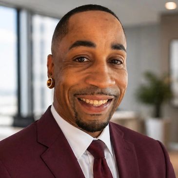 Smiling man in a maroon suit and tie indoors.