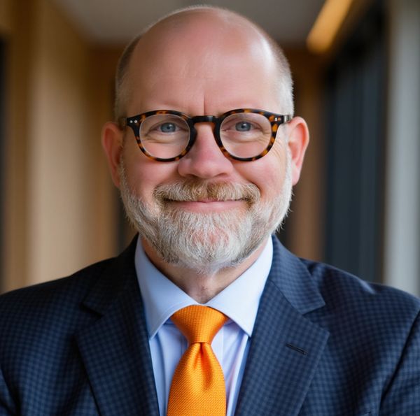 Smiling bald man with glasses in a suit and bright orange tie.