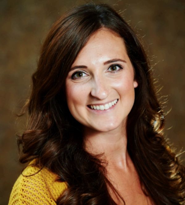 Smiling woman with long brown hair wearing a yellow sweater.