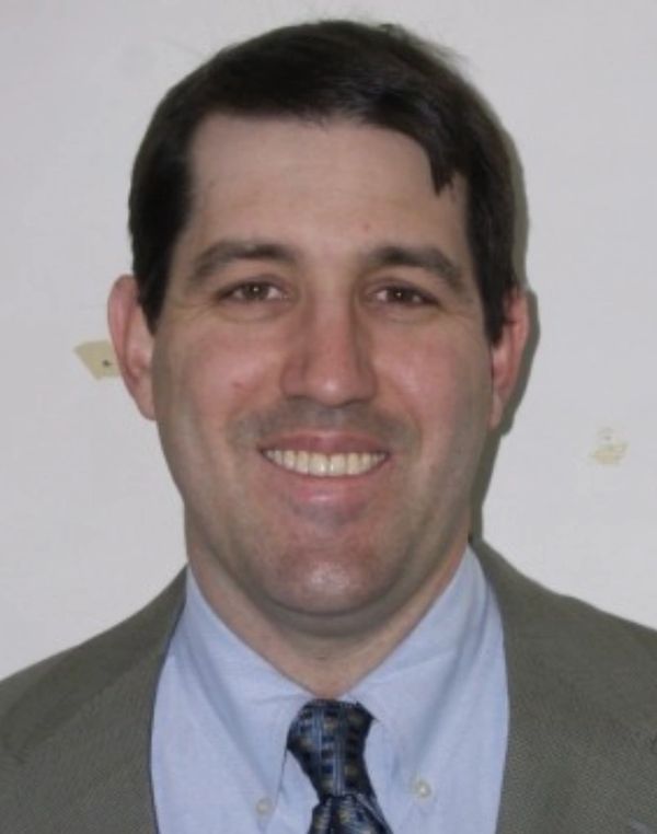 Smiling man in a suit and tie posing against a plain background.