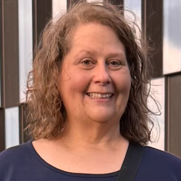 Smiling woman with curly hair standing outdoors in front of a building.