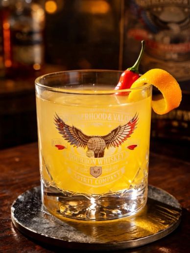 Whiskey cocktail garnished with chili and orange peel.